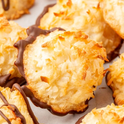 Close-up of a baked coconut macaroon with a chocolate-dipped base, surrounded by other macaroons.