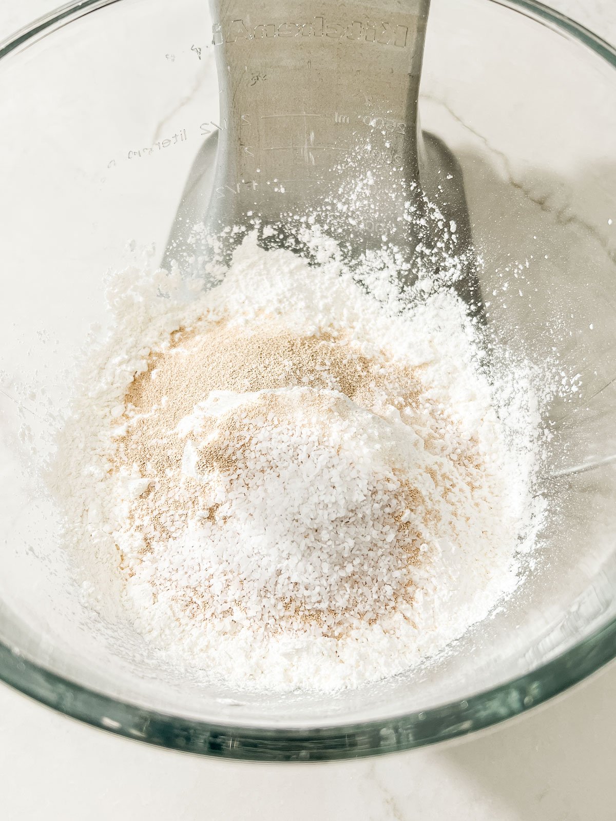 Dry ingredients including gluten-free flour, salt, and instant yeast in a glass mixing bowl.
