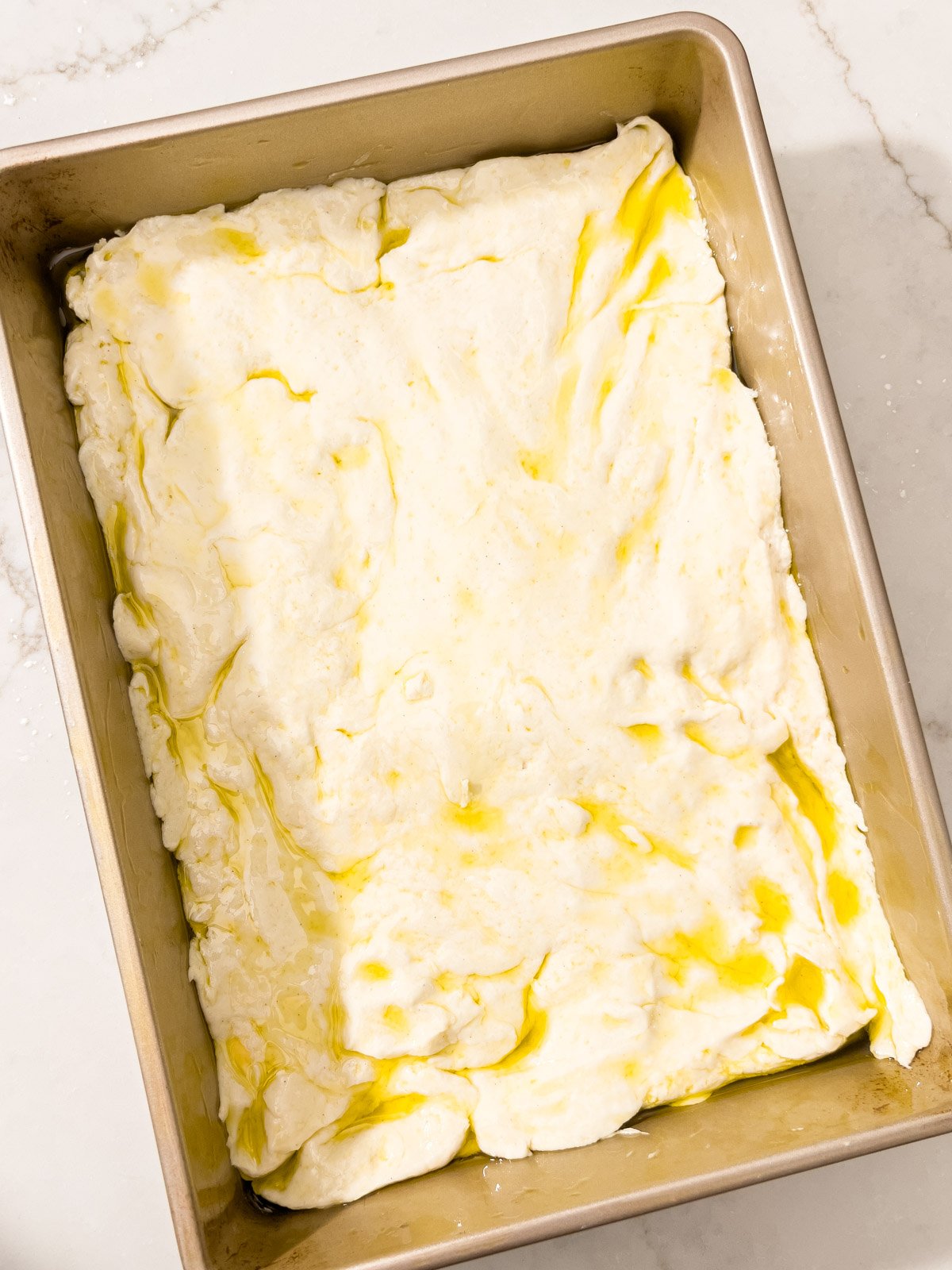 Focaccia dough spread out evenly in the pan, ready to rise.