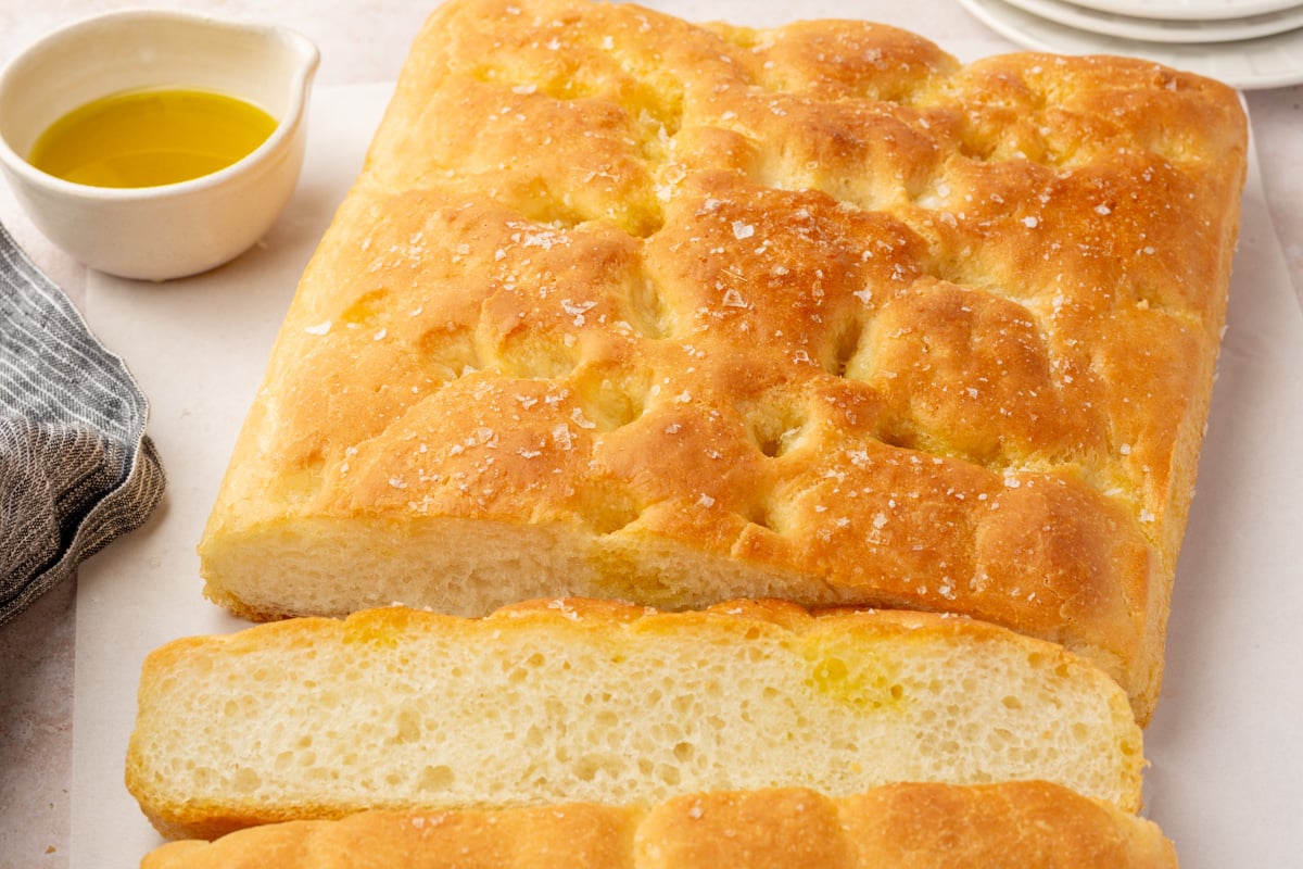 Detailed shot of the crusty edge of gluten-free focaccia dipped into olive oil and balsamic vinegar on a white plate.