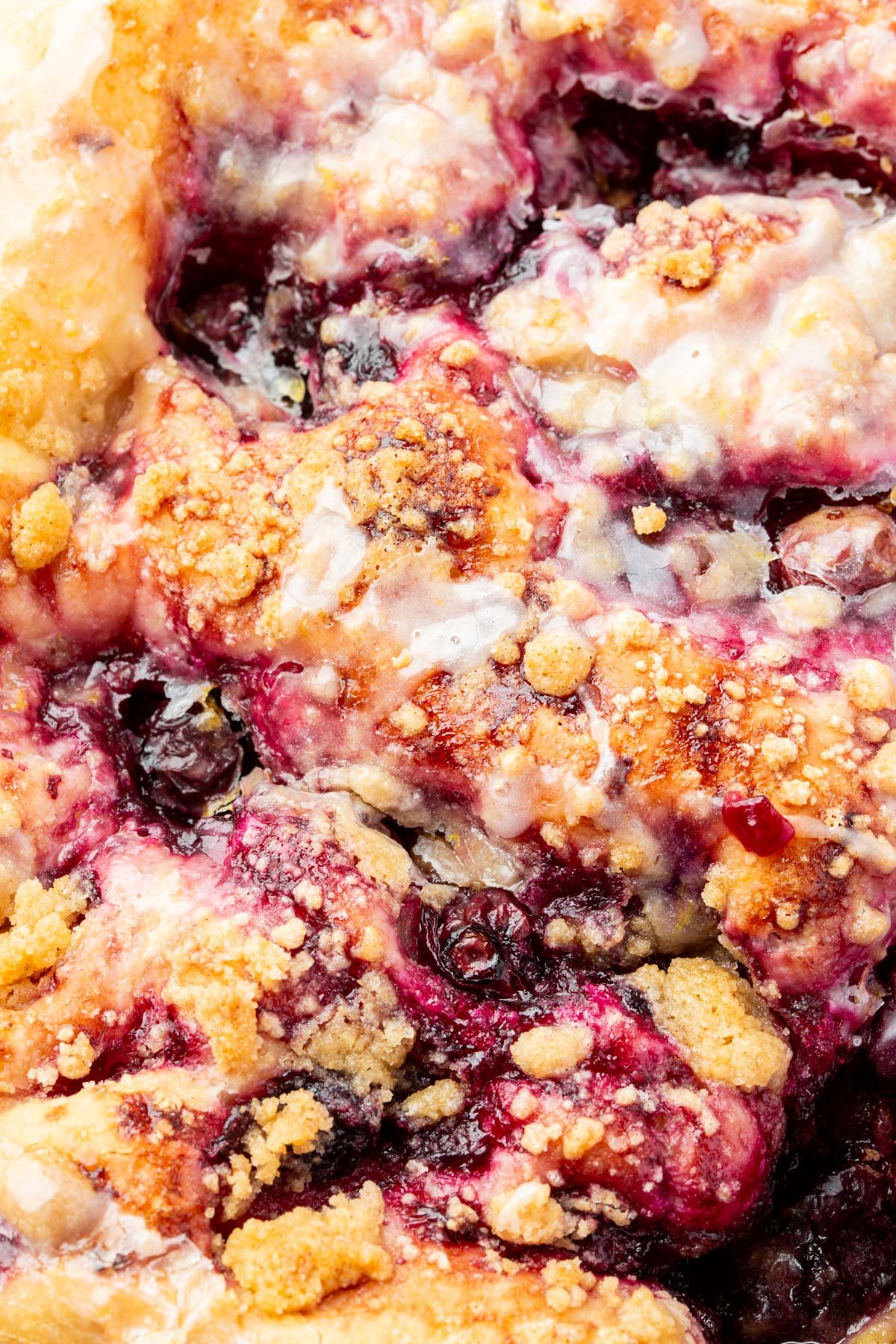 Macro shot of the baked crumble topping and thick blueberry compote on gluten-free focaccia, drizzled with lemon glaze.