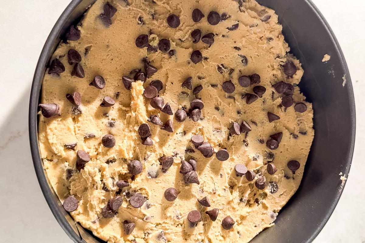 Unbaked gluten-free chocolate chip cookie cake dough pressed into a round pan and topped with extra chocolate chips.