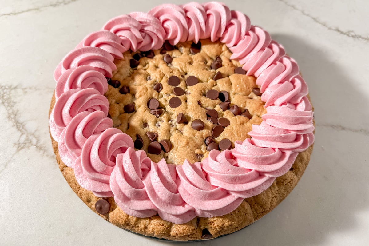 Finished gluten-free cookie cake with a thick border of pink frosting swirls piped around the edge.