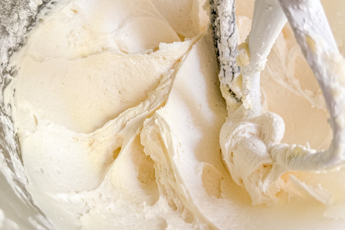 Whipped vanilla buttercream frosting in a mixing bowl with a paddle attachment.
