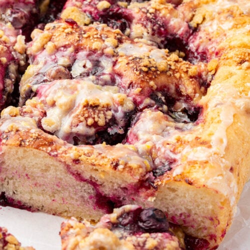 Partially sliced gluten-free blueberry crumble focaccia with visible lemon glaze, golden edges, and jammy blueberry filling.