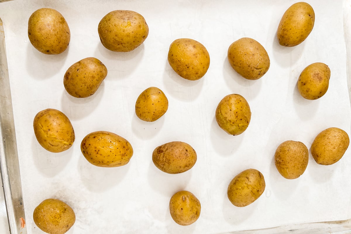 Cooked whole potatoes arranged on a parchment-lined baking sheet.