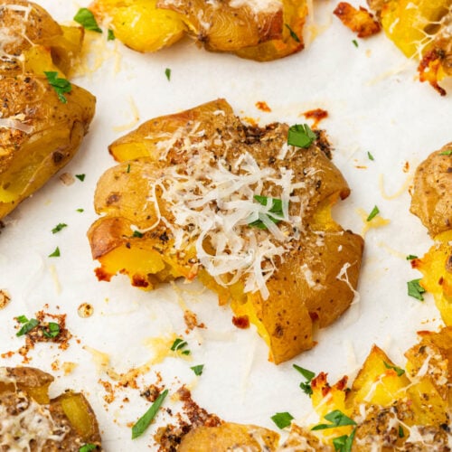 Close-up of a single smashed potato topped with melted parmesan and fresh parsley.
