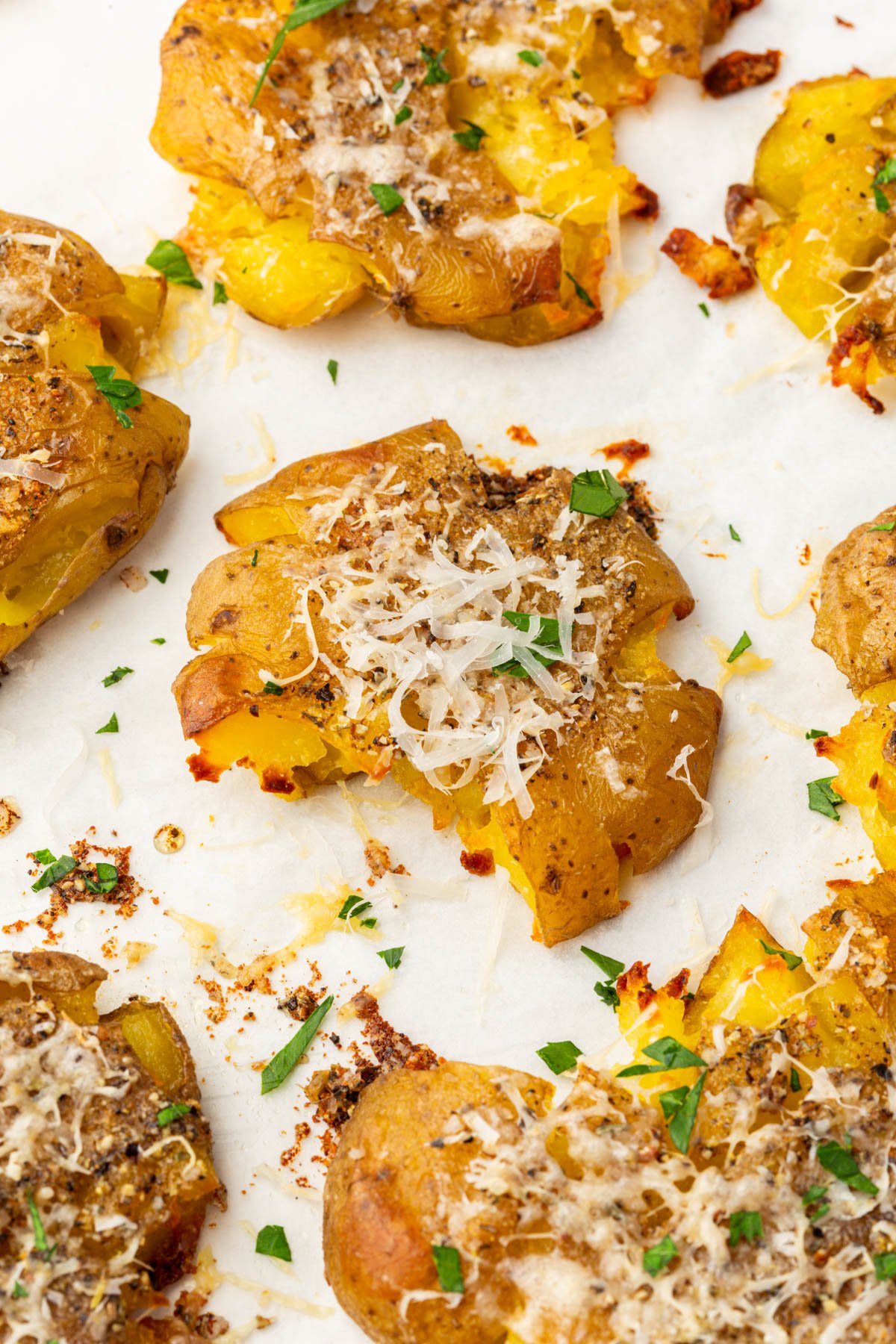 Close-up of a single smashed potato topped with melted parmesan and fresh parsley.