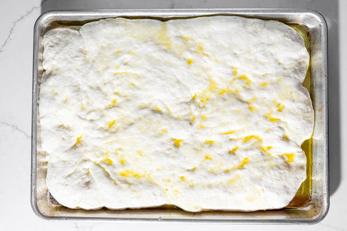 Gluten-free dough fully risen in a sheet pan before dimpling and seasoning.