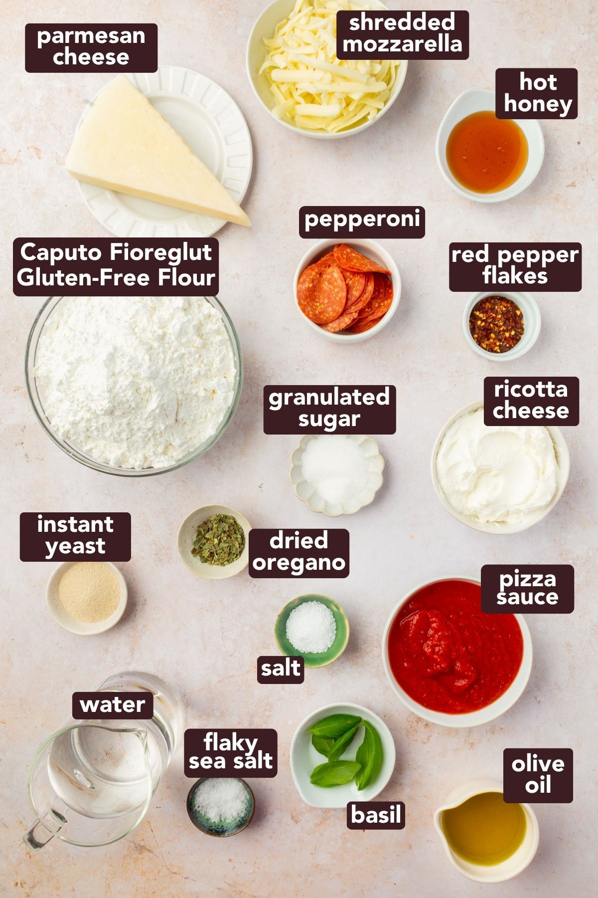 Overhead view of labeled ingredients for gluten-free focaccia pizza, including flour, cheese, pepperoni, and herbs.