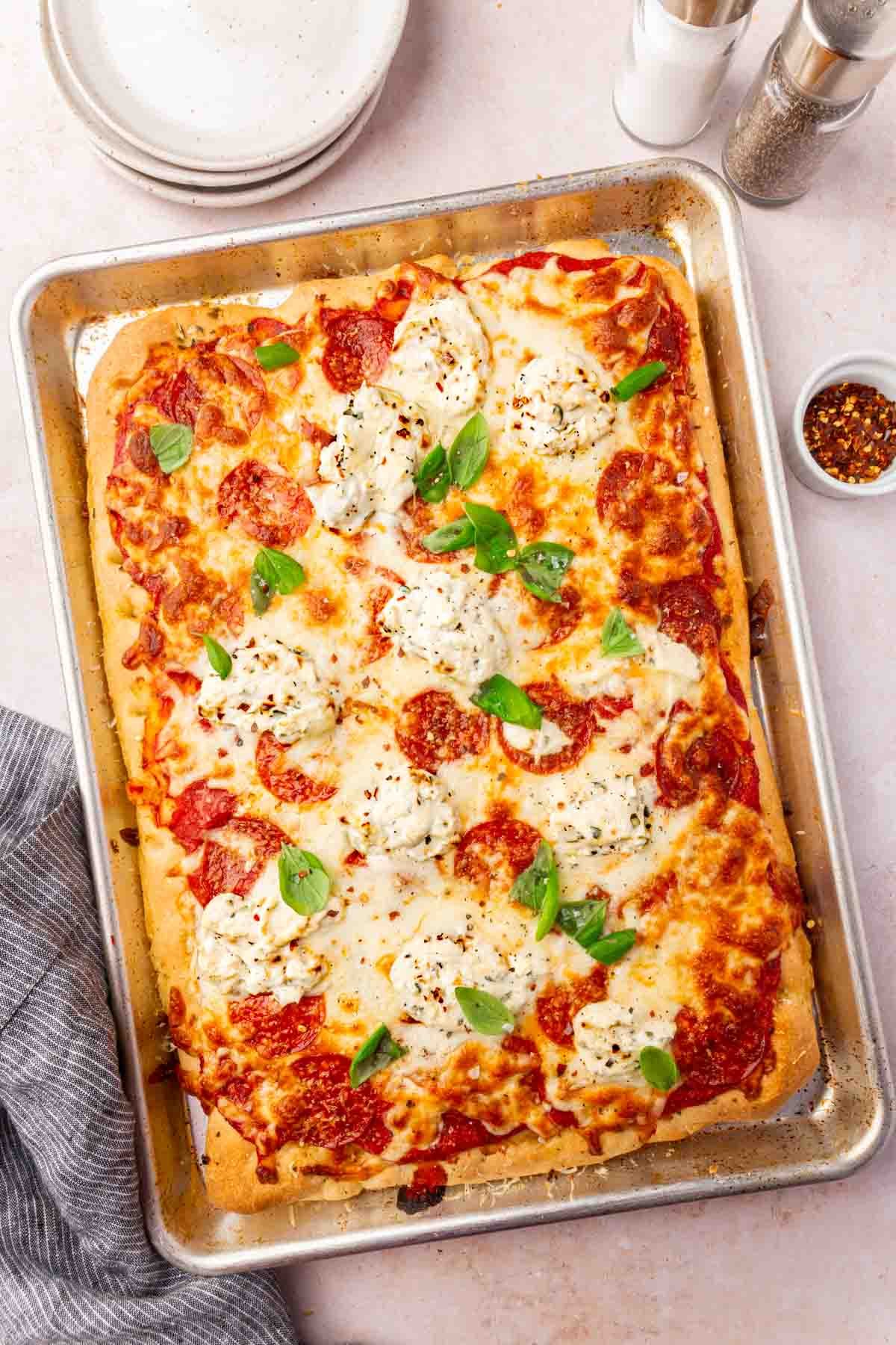 Overhead view of baked gluten-free focaccia pizza in pan with plates and red pepper flakes on the side.