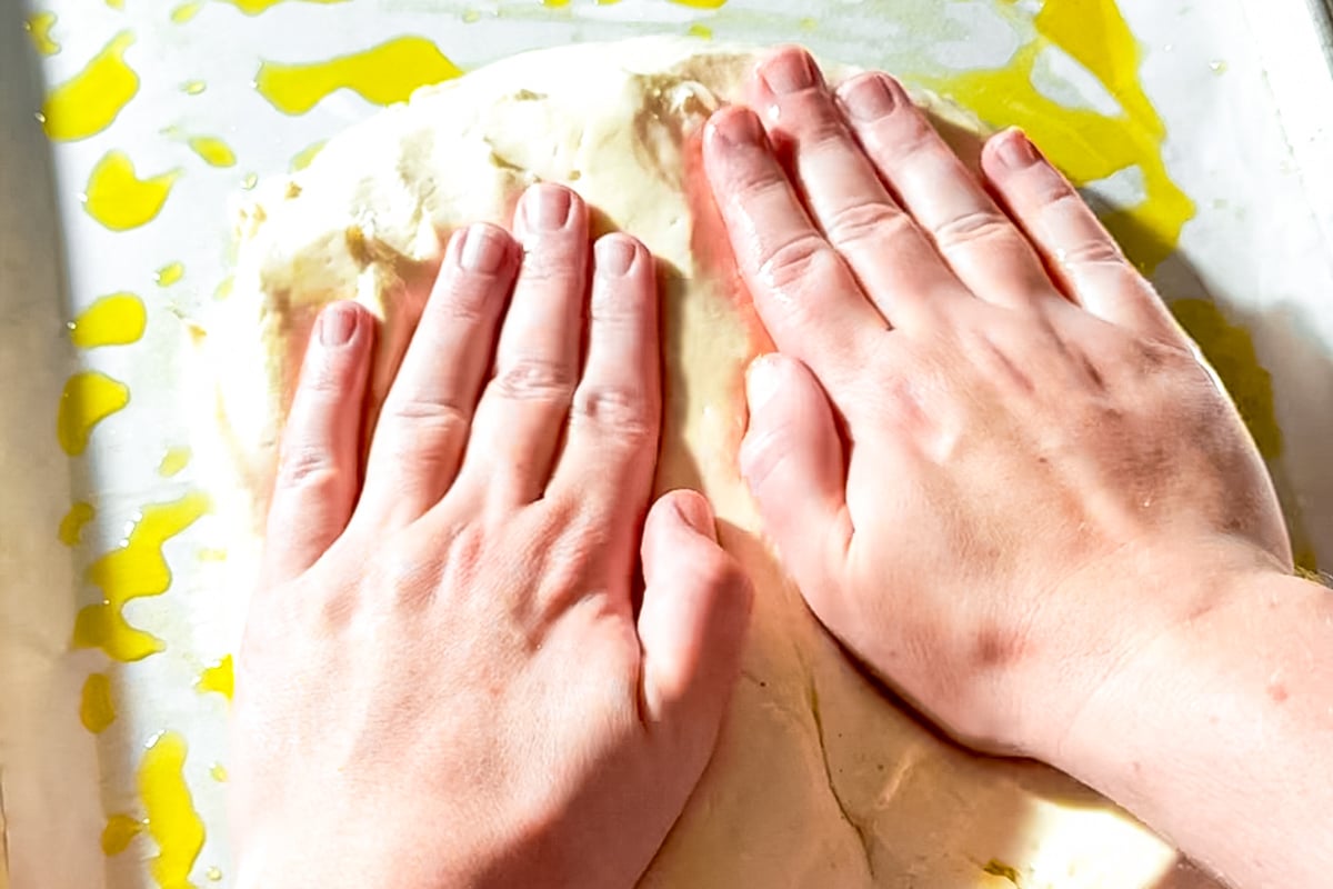Oiled hands pressing gluten-free dough into a sheet pan before rising.