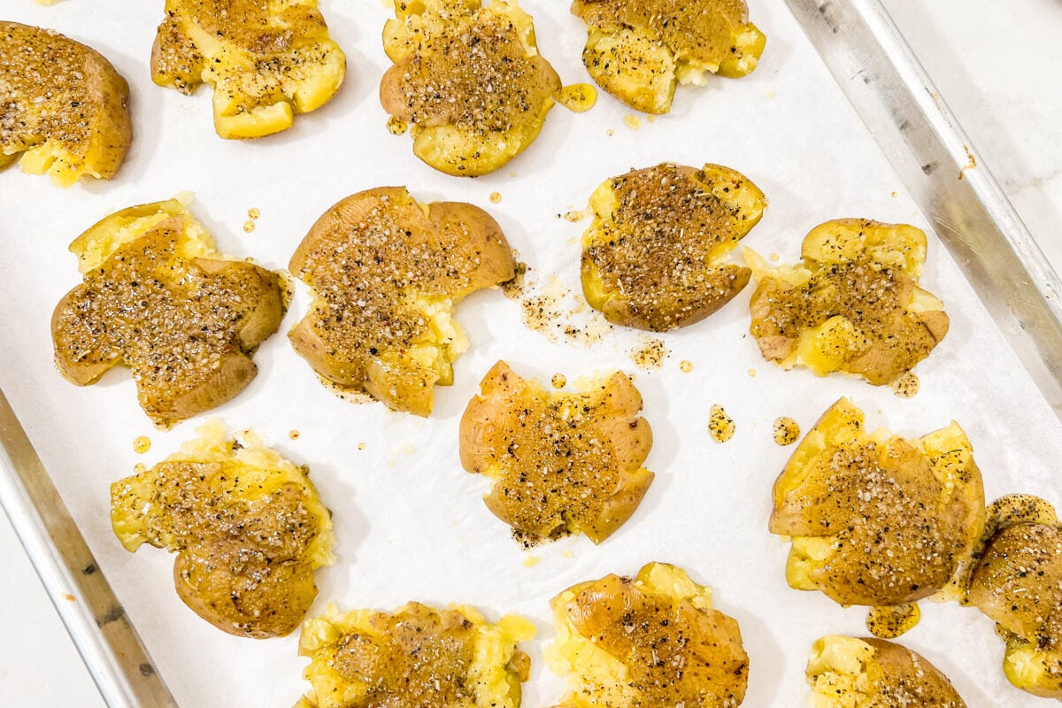 Smashed potatoes sprinkled with salt, pepper, and oil before roasting.
