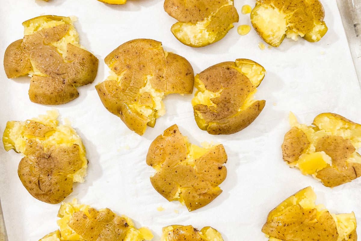 Boiled potatoes smashed flat on a baking sheet, ready for seasoning.