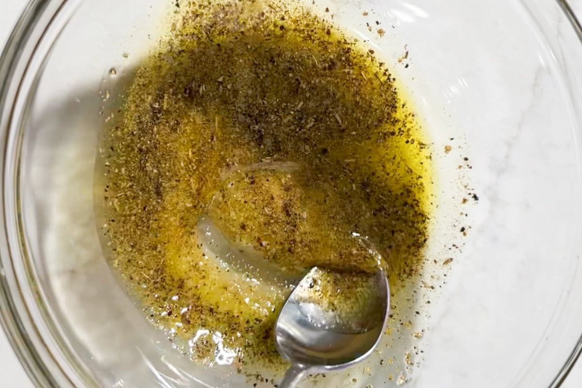 A glass mixing bowl with olive oil, salt, pepper, Italian seasoning and garlic powder.