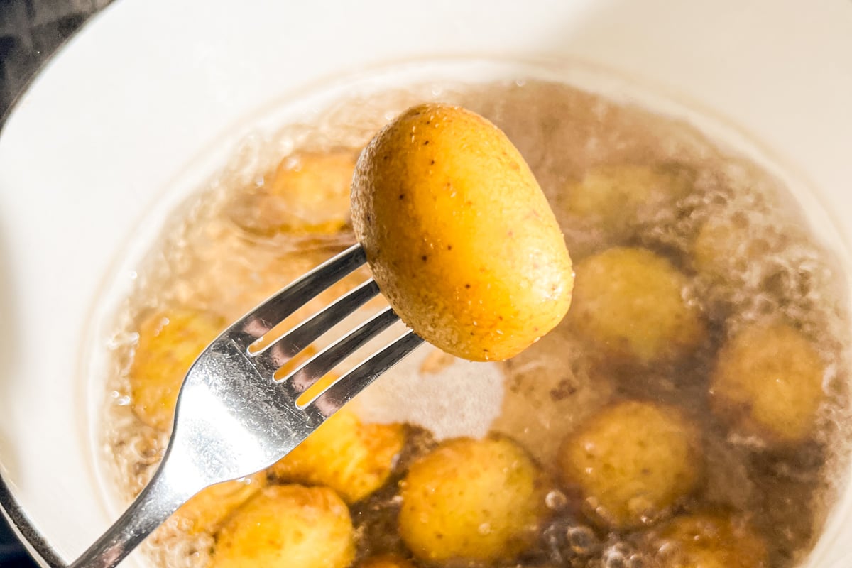 Fork holding a boiled potato over a bubbling pot to test tenderness.