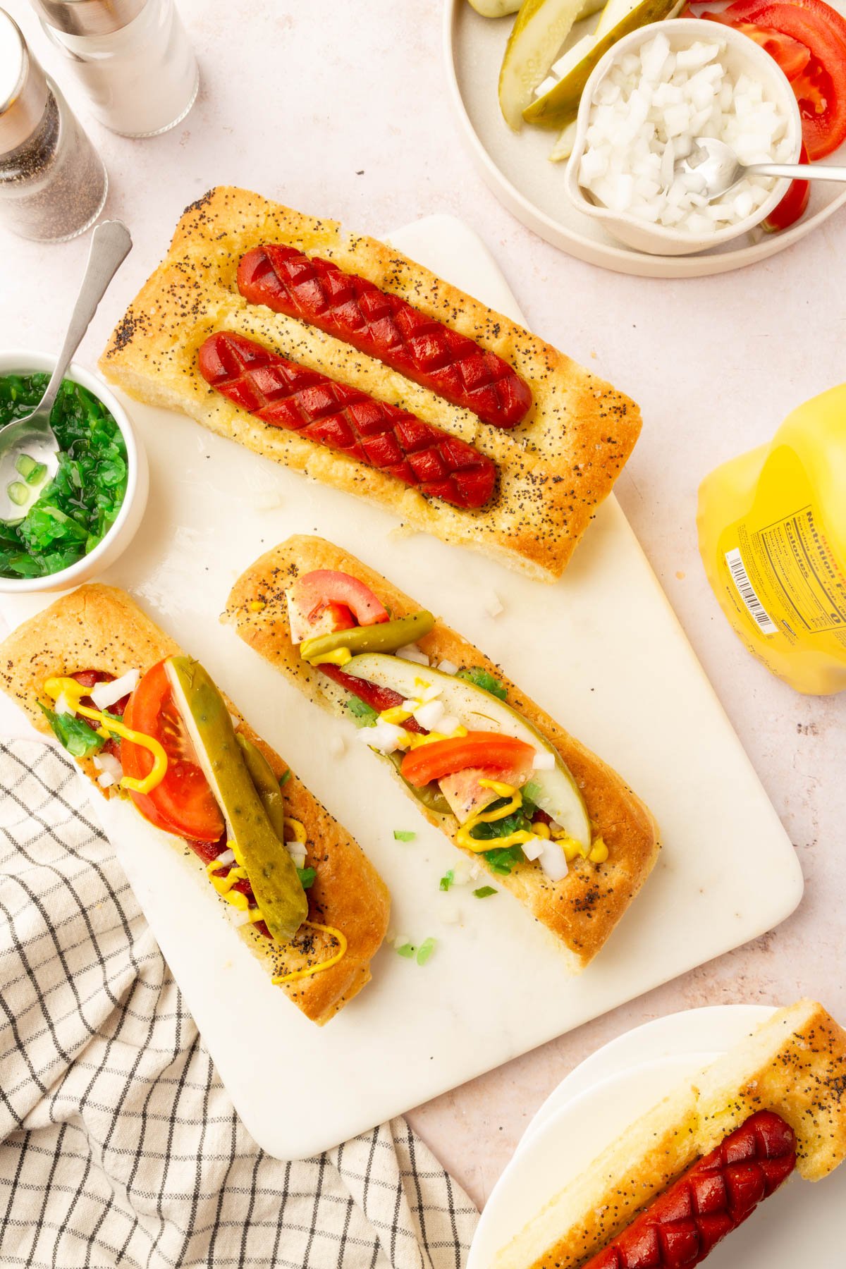 Overhead view of sliced gluten-free hot dog focaccia with toppings like tomatoes, pickles, mustard, and relish.