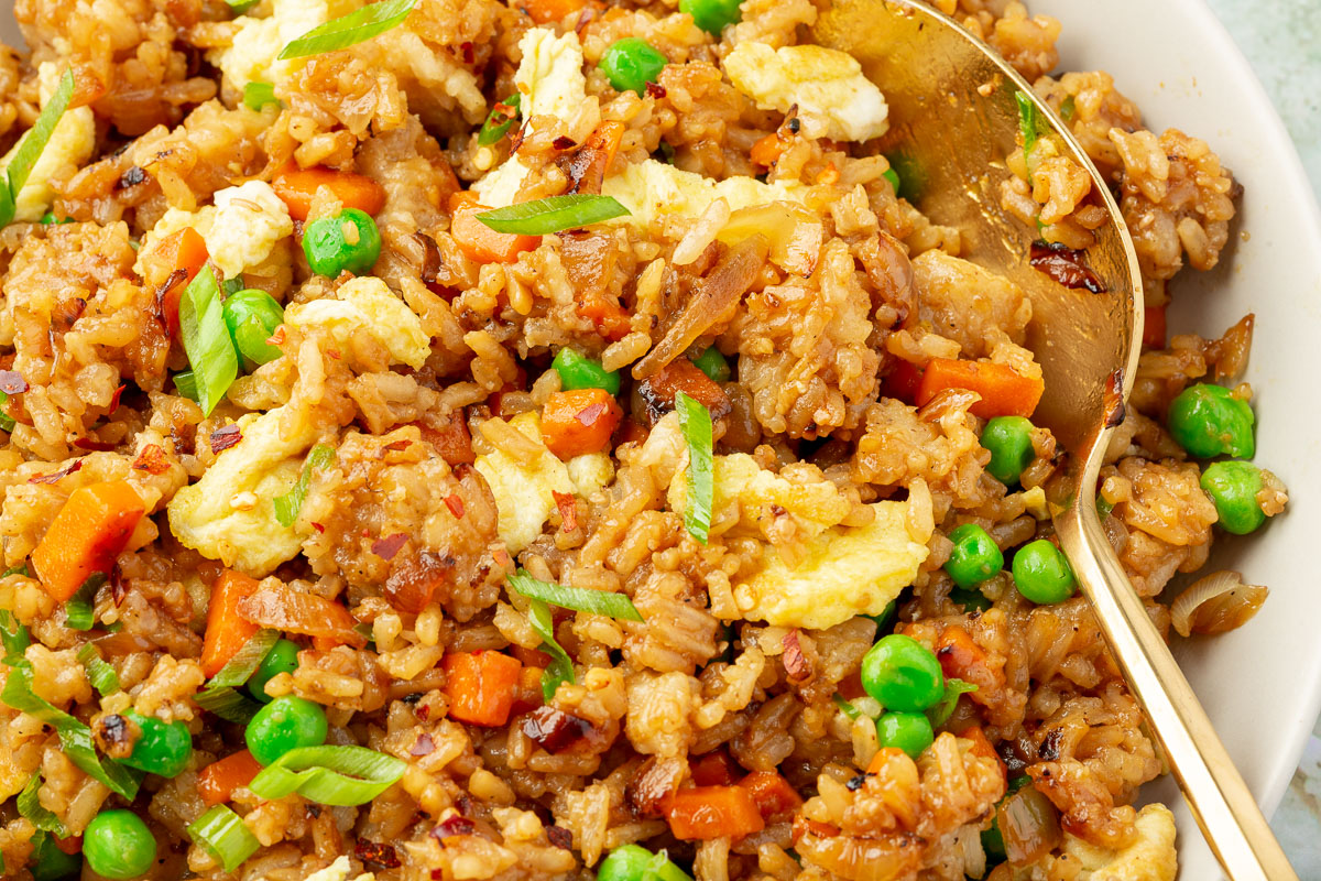 Close-up view of gluten-free fried rice showing scrambled eggs, green peas, carrots, and green onions.