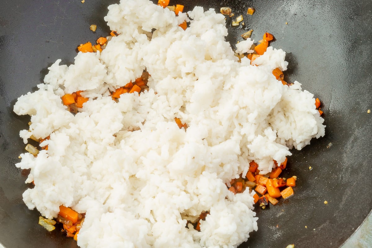 Steamed white rice added to vegetables in the wok for gluten-free fried rice.