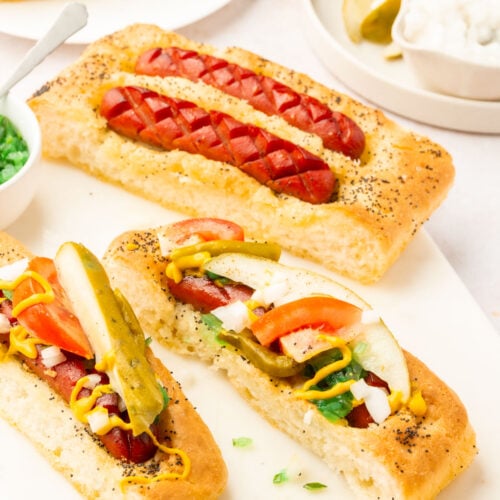 Gluten-free focaccia hot dogs topped with classic Chicago-style toppings like sport peppers, tomato, and relish.