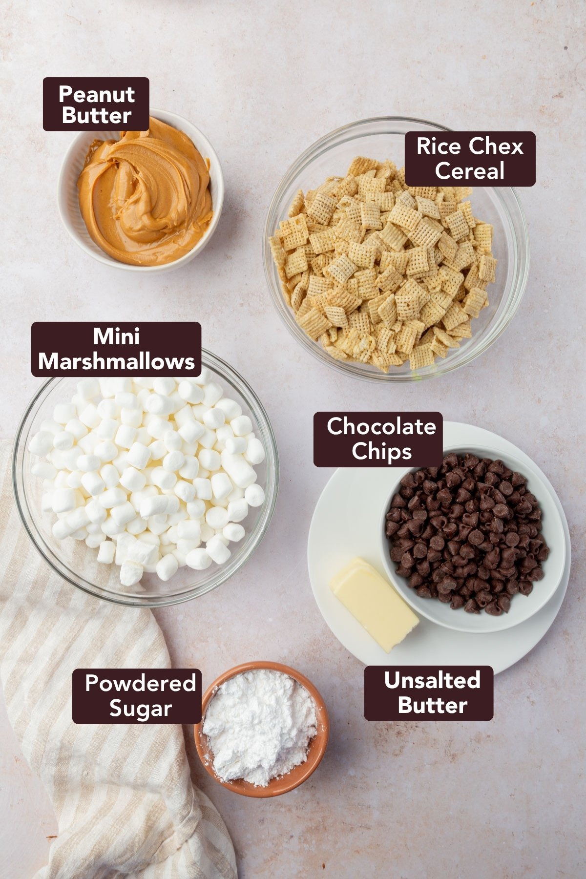 Ingredients for puppy chow bars including peanut butter, Chex cereal, mini marshmallows, chocolate chips, butter, and powdered sugar in labeled bowls.