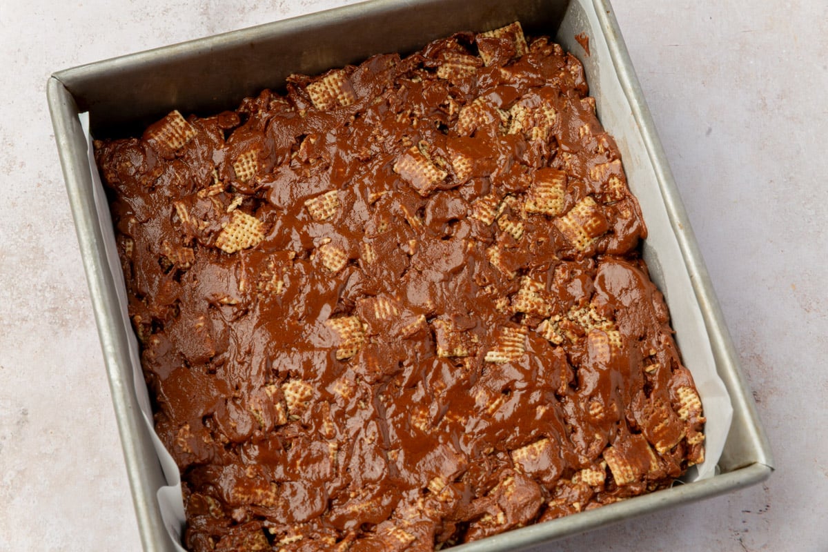 Chocolate cereal mixture evenly pressed into a square baking pan lined with parchment paper.