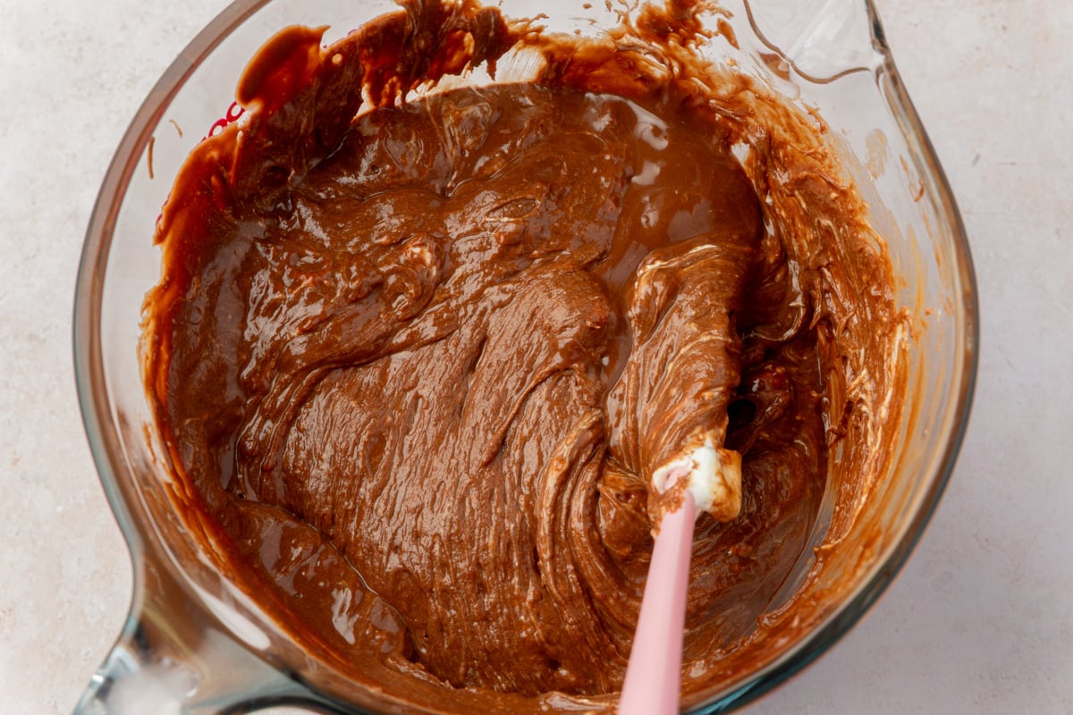 Melted chocolate, peanut butter, and marshmallow mixture in a glass bowl with a pink spatula mid-stir.