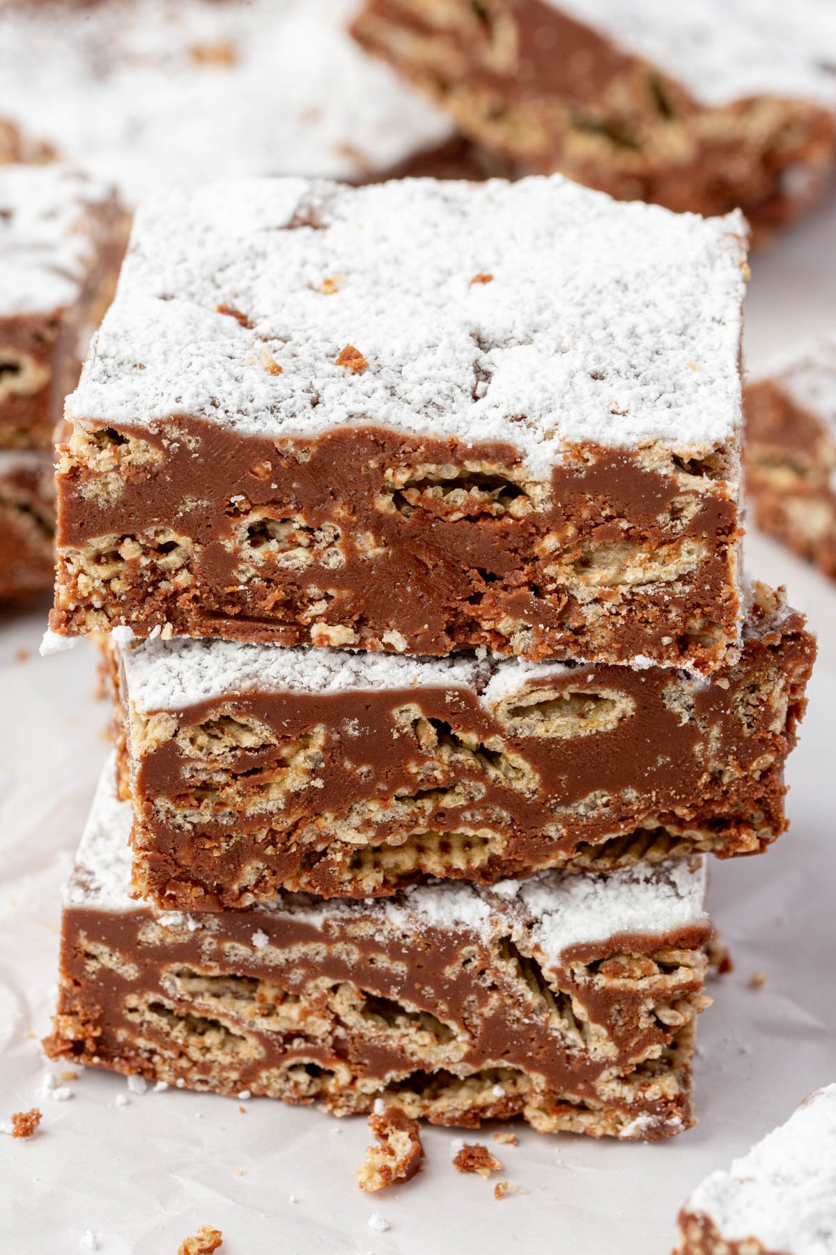 Close-up of three muddy buddy bars stacked on top of each other, showing a cross-section of Chex cereal coated in chocolate and dusted with powdered sugar.