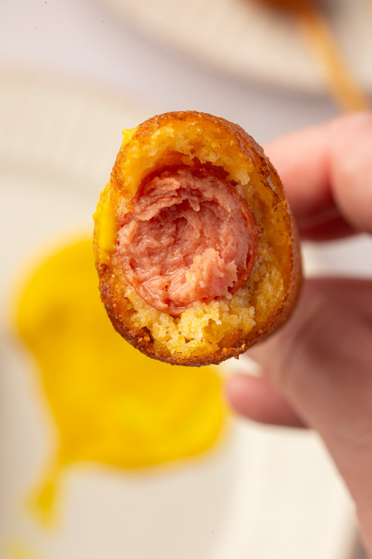 Close-up of a bitten gluten-free corn dog showing the hot dog inside and golden crispy cornmeal batter.