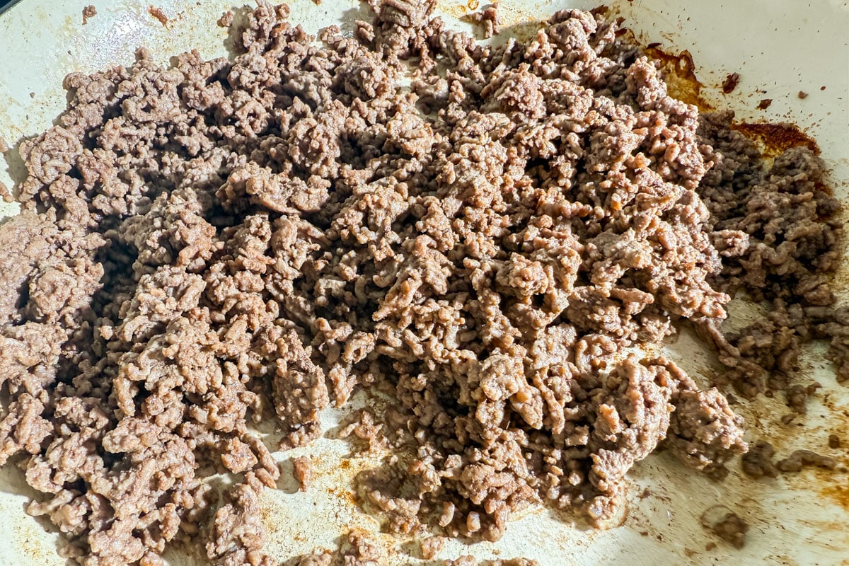 Skillet with browned ground beef for gluten-free taco salad.