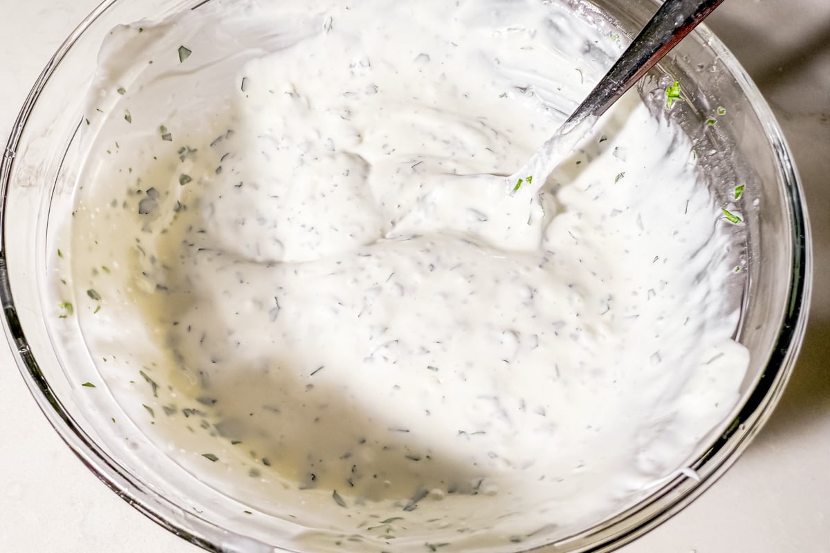 A bowl of cilantro lime dressing with a spoon after being mixed together.