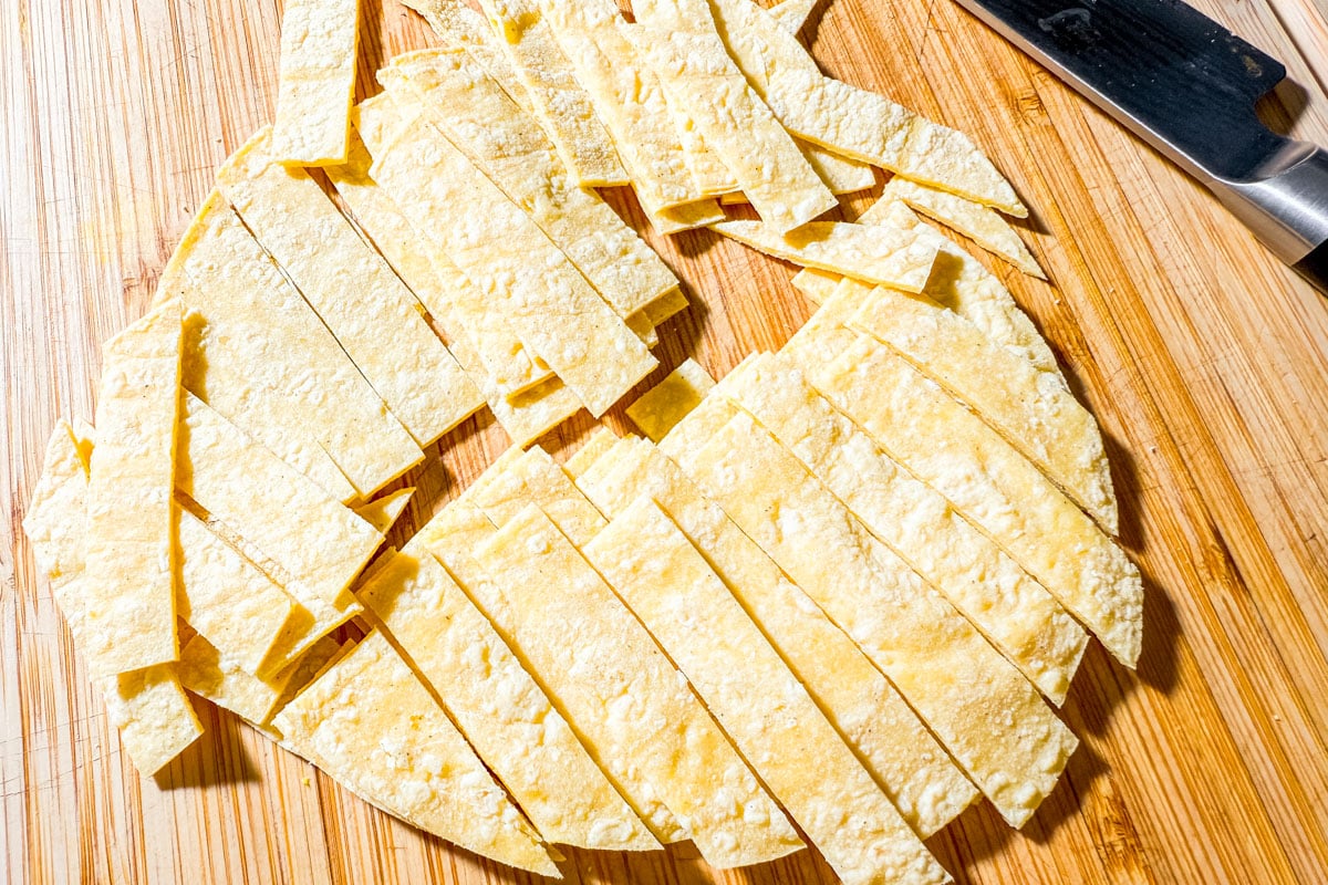 Corn tortillas cut into thin strips on a cutting board, ready to fry for taco salad.