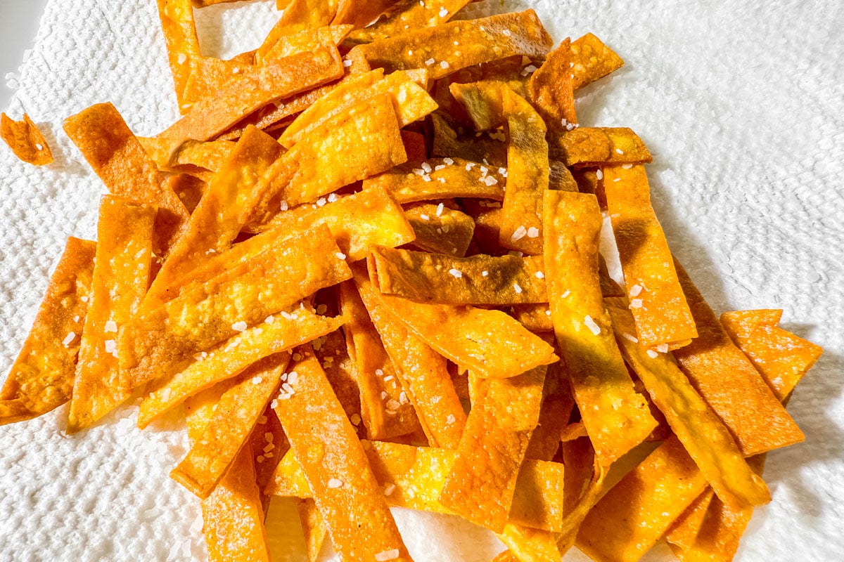Golden fried corn tortilla strips sprinkled with salt, draining on paper towel.