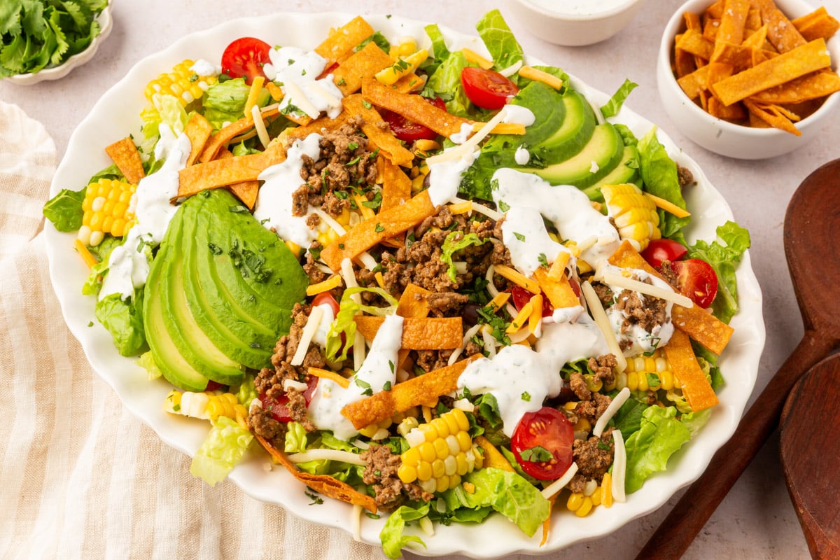 Overhead view of a gluten-free taco salad topped with ground beef, avocado slices, corn, tomatoes, and crispy tortilla strips with cilantro lime dressing.