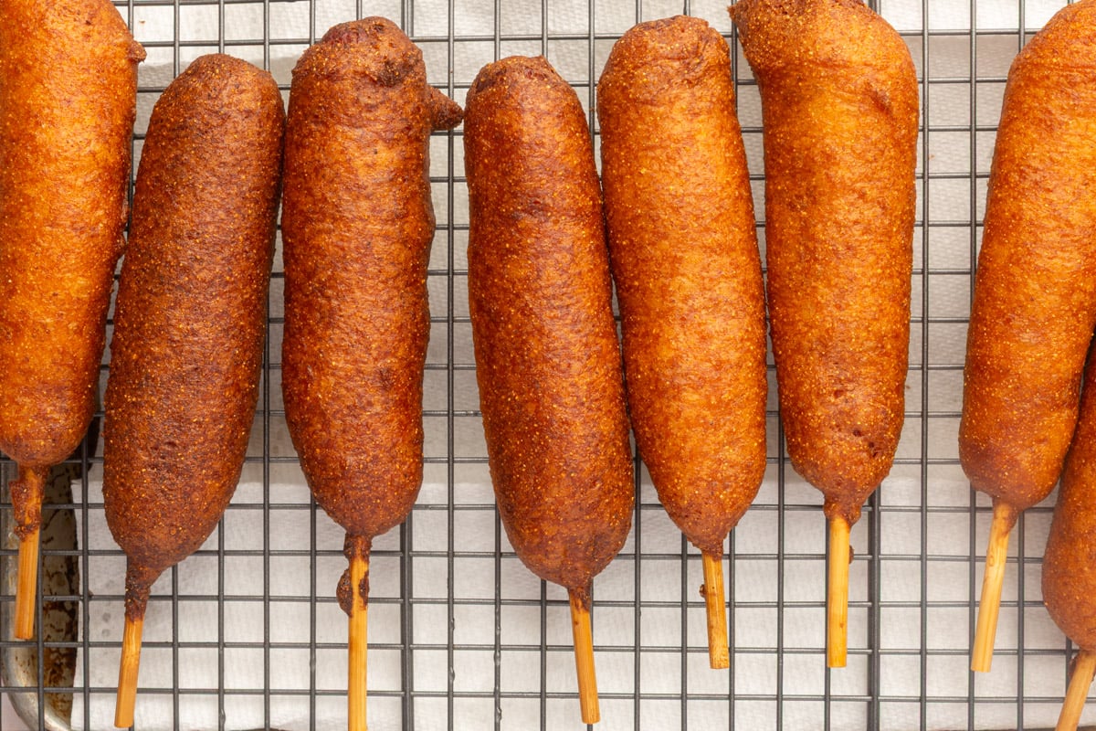 Freshly fried gluten-free corn dogs cooling on a wire rack over paper towels.