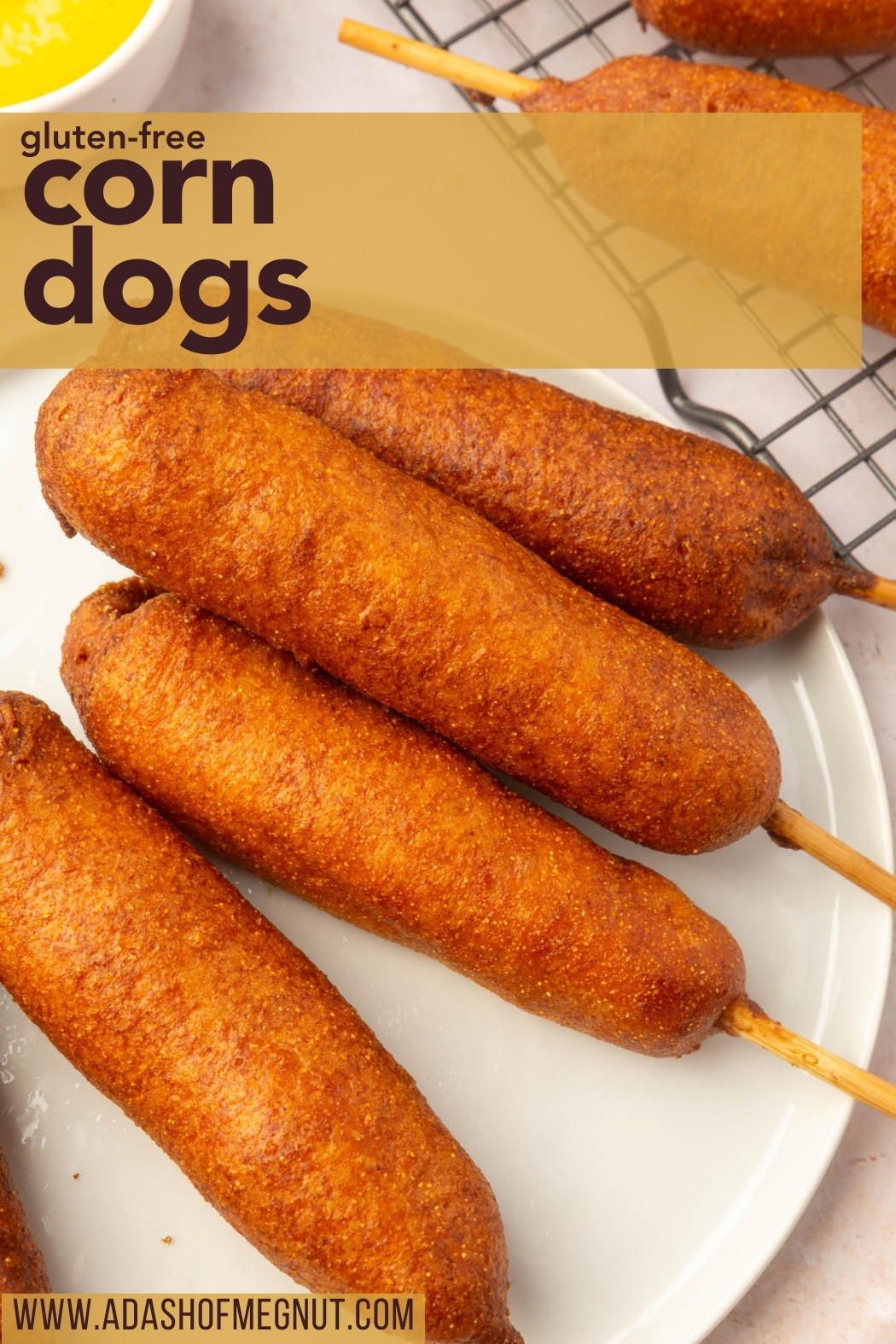 Stack of golden gluten-free corn dogs on a white plate with mustard in the background.
