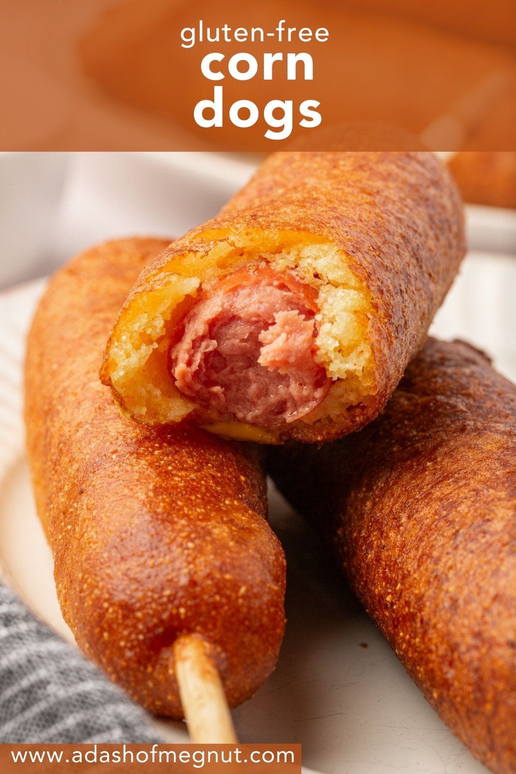Gluten-free corn dog with a bite taken out stacked on top of another corn dog, showing the hot dog inside.
