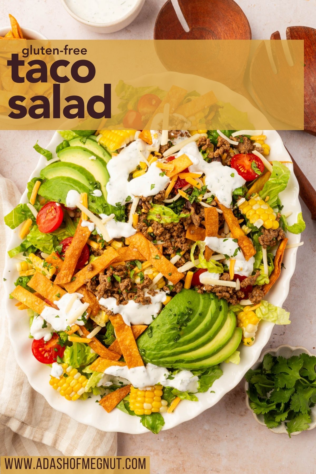 Fresh gluten-free taco salad topped with beef, cheese, avocado, corn, and tortilla strips, styled with wood serving spoons for Pinterest.