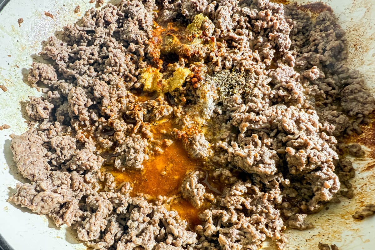 Ground beef cooking in skillet with taco seasoning and spices.