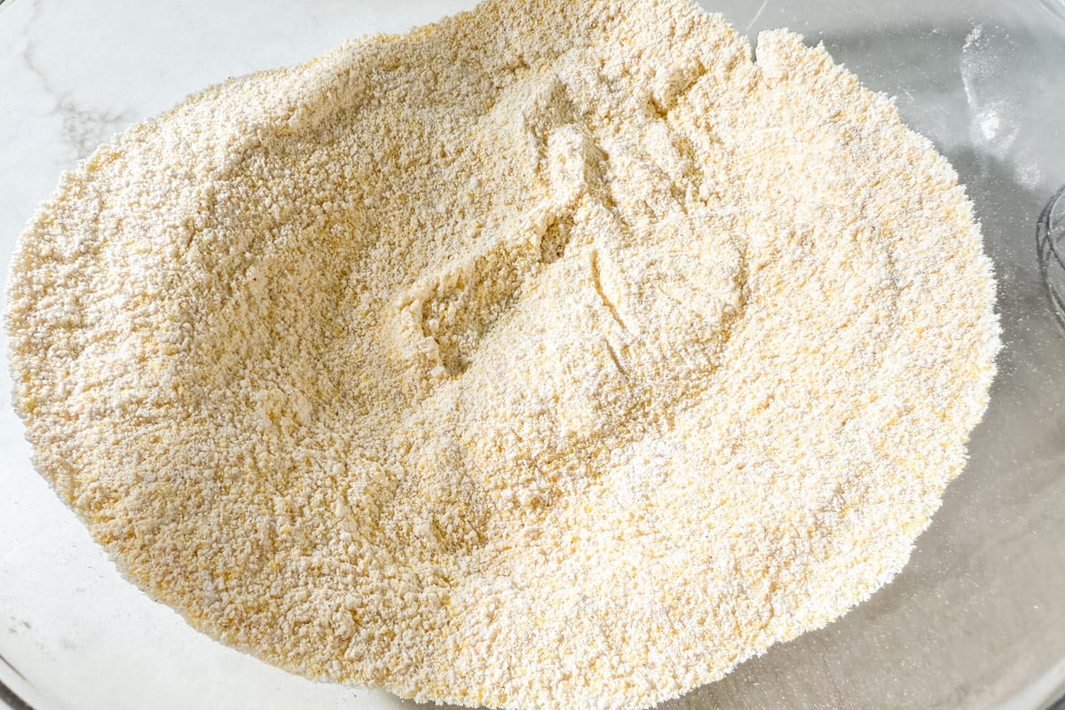 A bowl of combined dry ingredients for gluten-free corn dogs, including cornmeal and gluten-free flour.