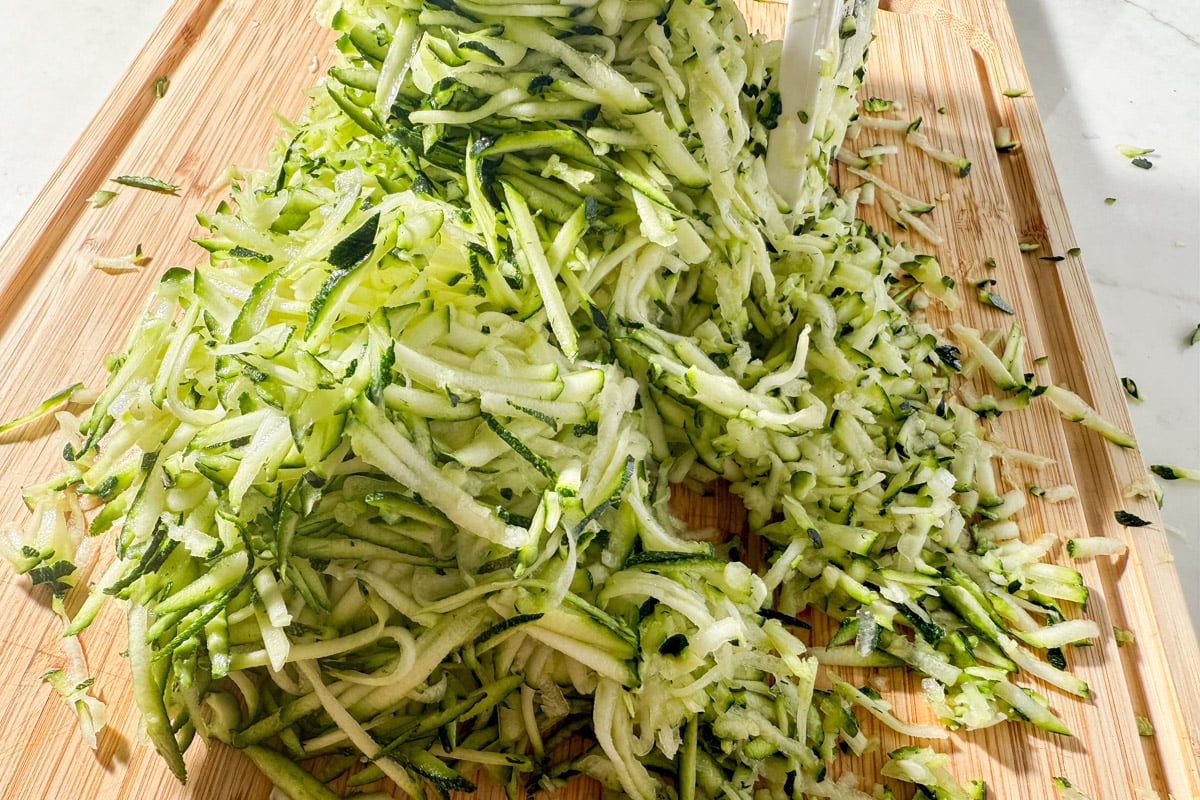 Pile of shredded zucchini spread across a wooden cutting board.