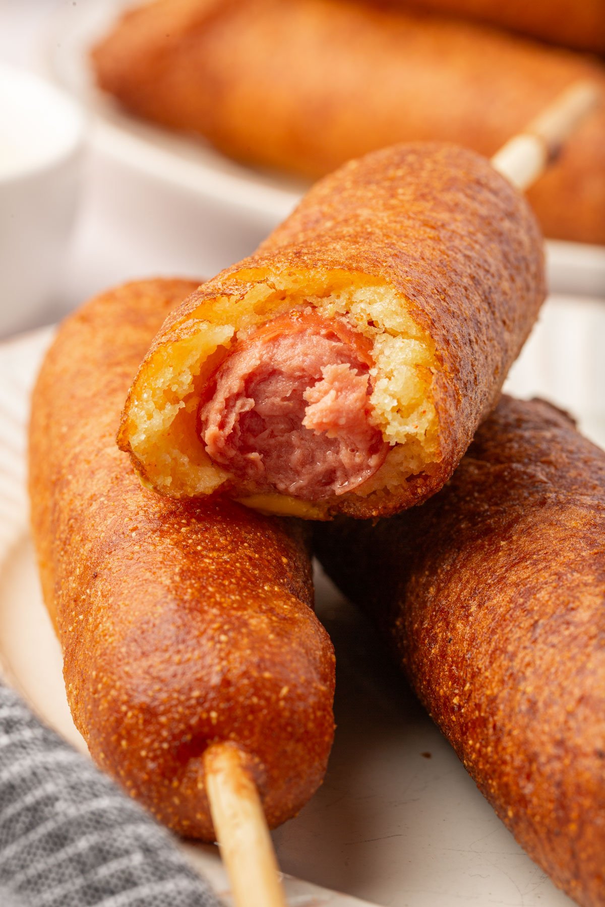 Close-up of stacked gluten-free corn dogs with one bitten to reveal the hot dog inside.