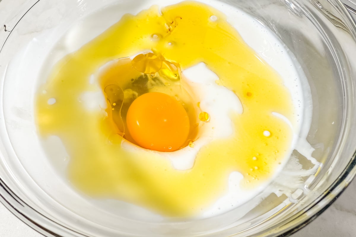 Egg, oil, and milk in a glass mixing bowl for gluten-free corn dog batter.