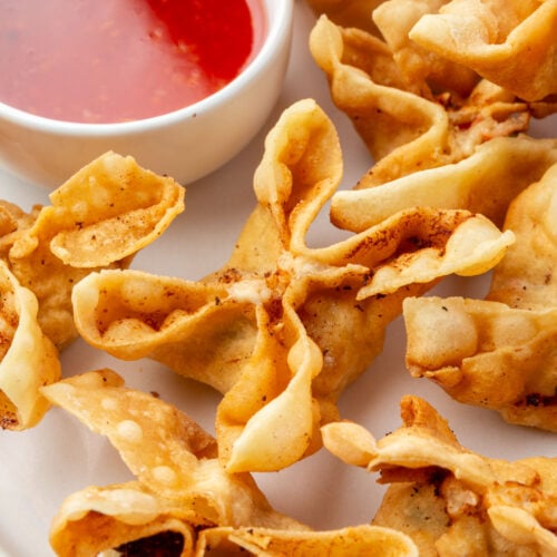 A plate of crispy gluten-free crab rangoons served with a bowl of sweet and sour dipping sauce.