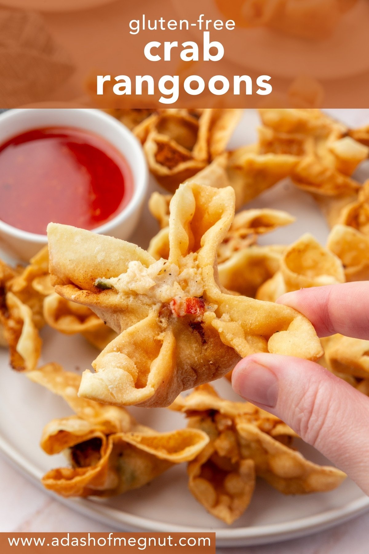 A hand holding a golden gluten-free crab rangoon with sweet and sour dipping sauce in the background.