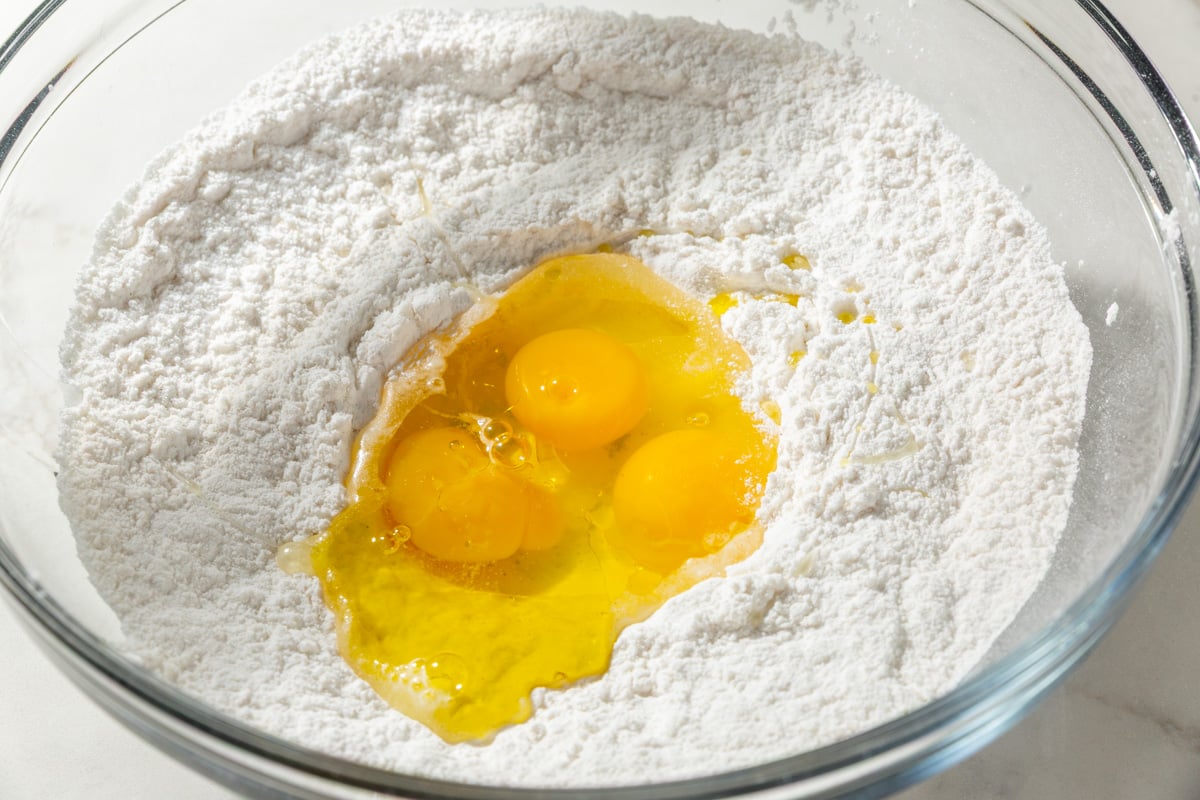 Three raw eggs cracked into the center of gluten-free flour in a mixing bowl, ready to combine for wonton dough.