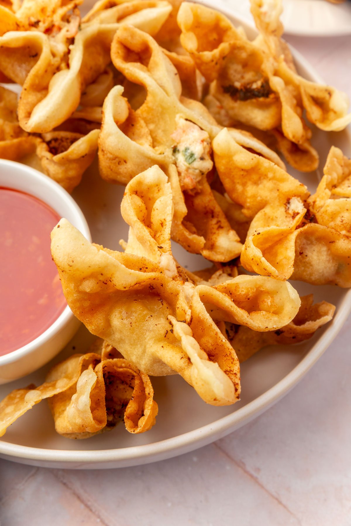 A plate piled high with golden brown gluten-free crab rangoons next to a bowl of dipping sauce.