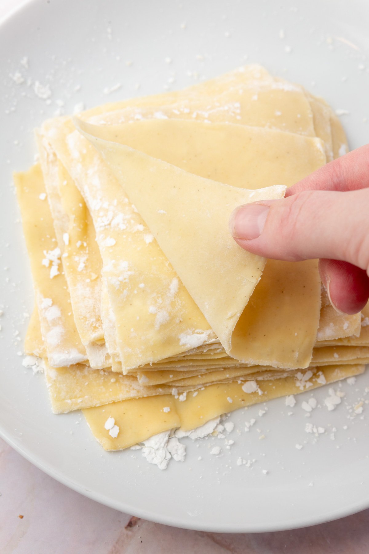 Hand peeling apart thin sheets of homemade gluten-free wonton wrappers on a white plate.
