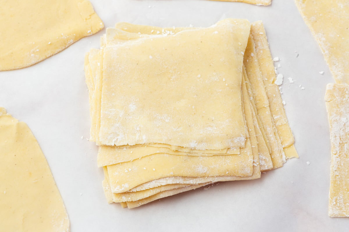 Stack of homemade gluten-free wonton wrappers lightly dusted with flour on parchment paper.