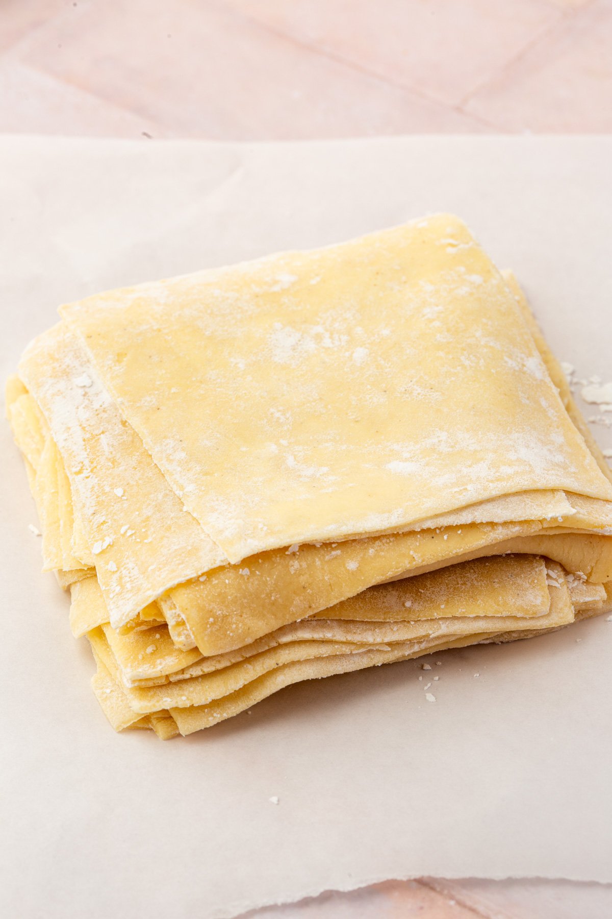 Neat stack of square gluten-free wonton wrappers on a floured surface, ready to use.
